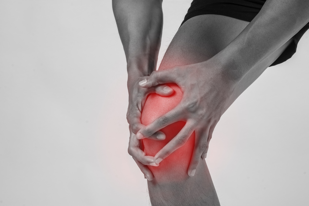 Young sport man with strong athletic legs holding knee with his hands in pain after suffering ligament injury  isolated on white.